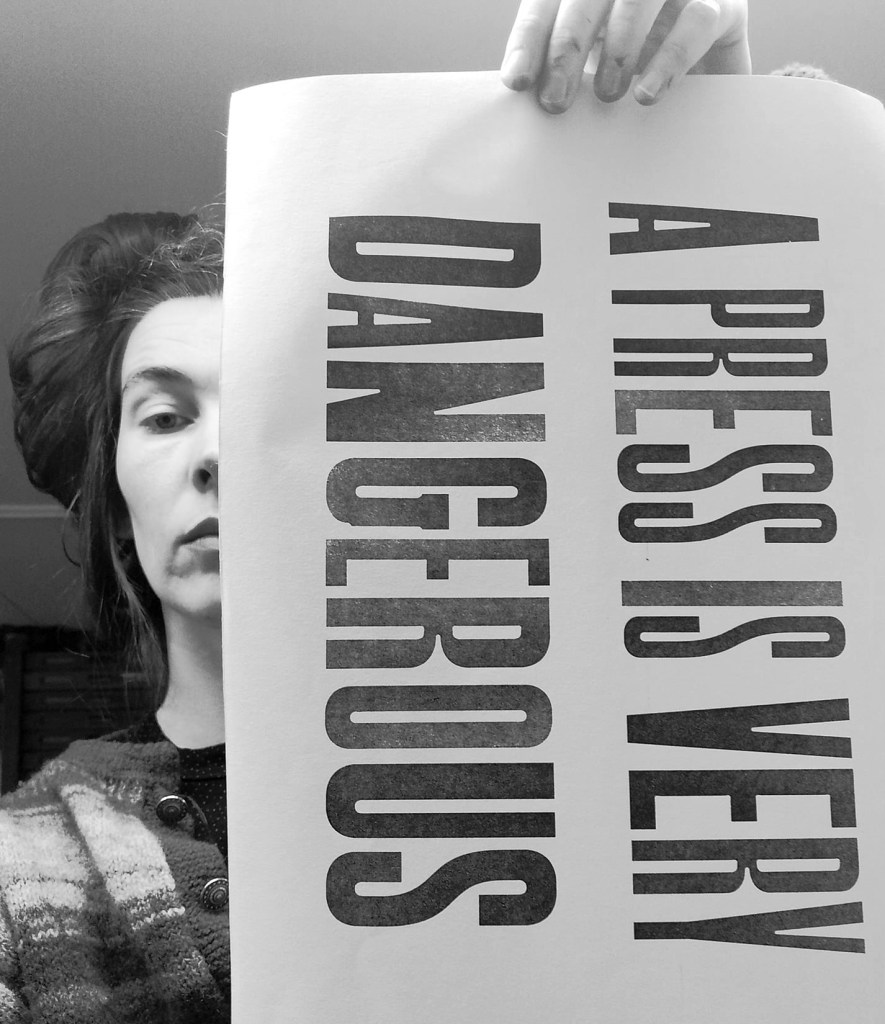 Artist Ane Thon Knutson holds a sheet of printed text stating 'A press is very dangerous'